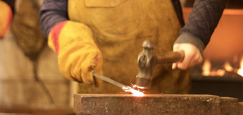 Ein Mädchen haut mit einem Hammer auf ein glühendes Stück Metall.