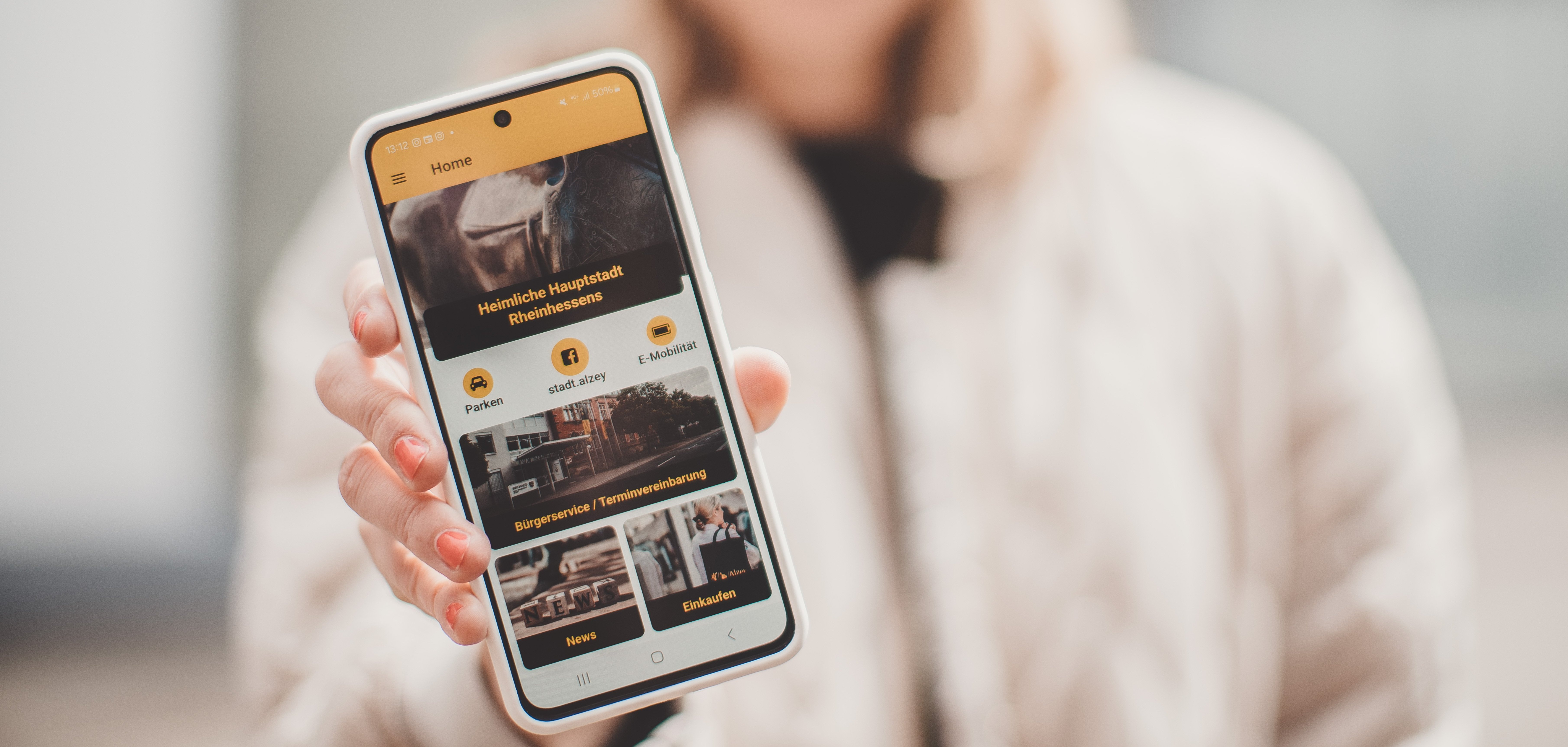 eine Frau zeigt die Startseite der Alzeyer Stadt App