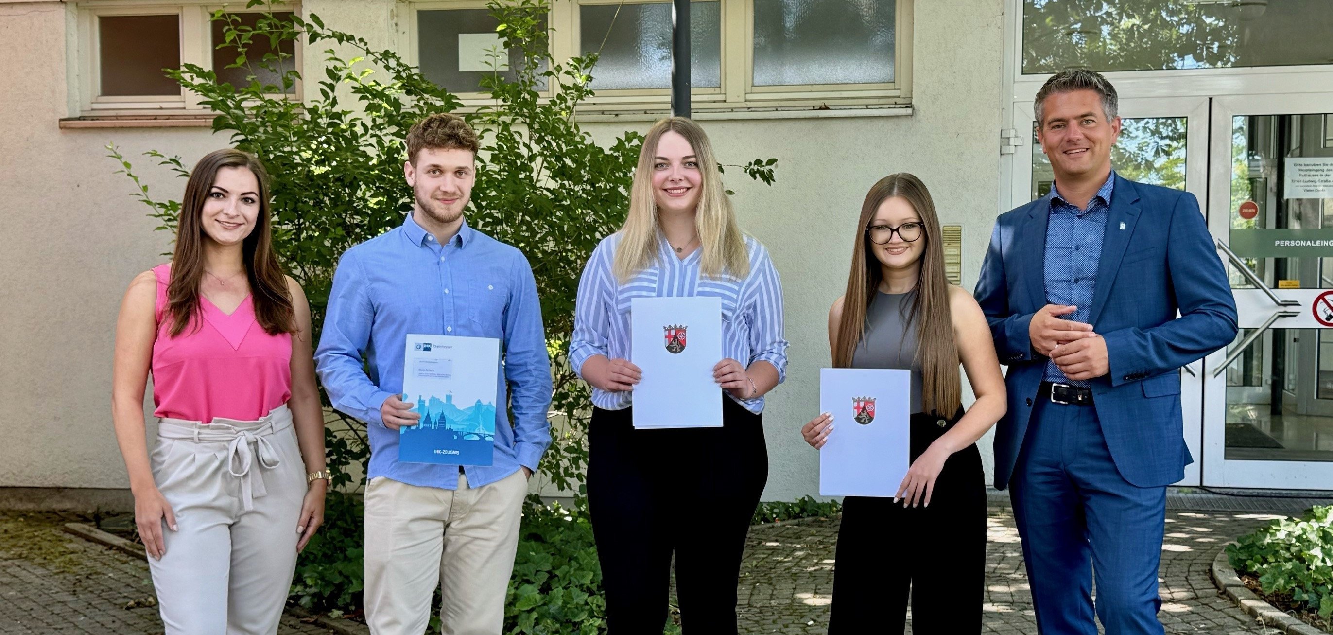 Fünf Personen stehen zusammen. Drei Personen in der Mitte halten ihre Zeugnisse in den Händen.