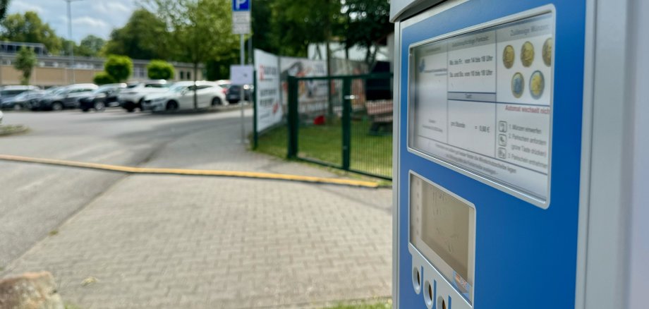 Ein Parkscheinautomat. Im Hintergrund stehen Autos vor dem Eingangsbereich des Wartbergbads.