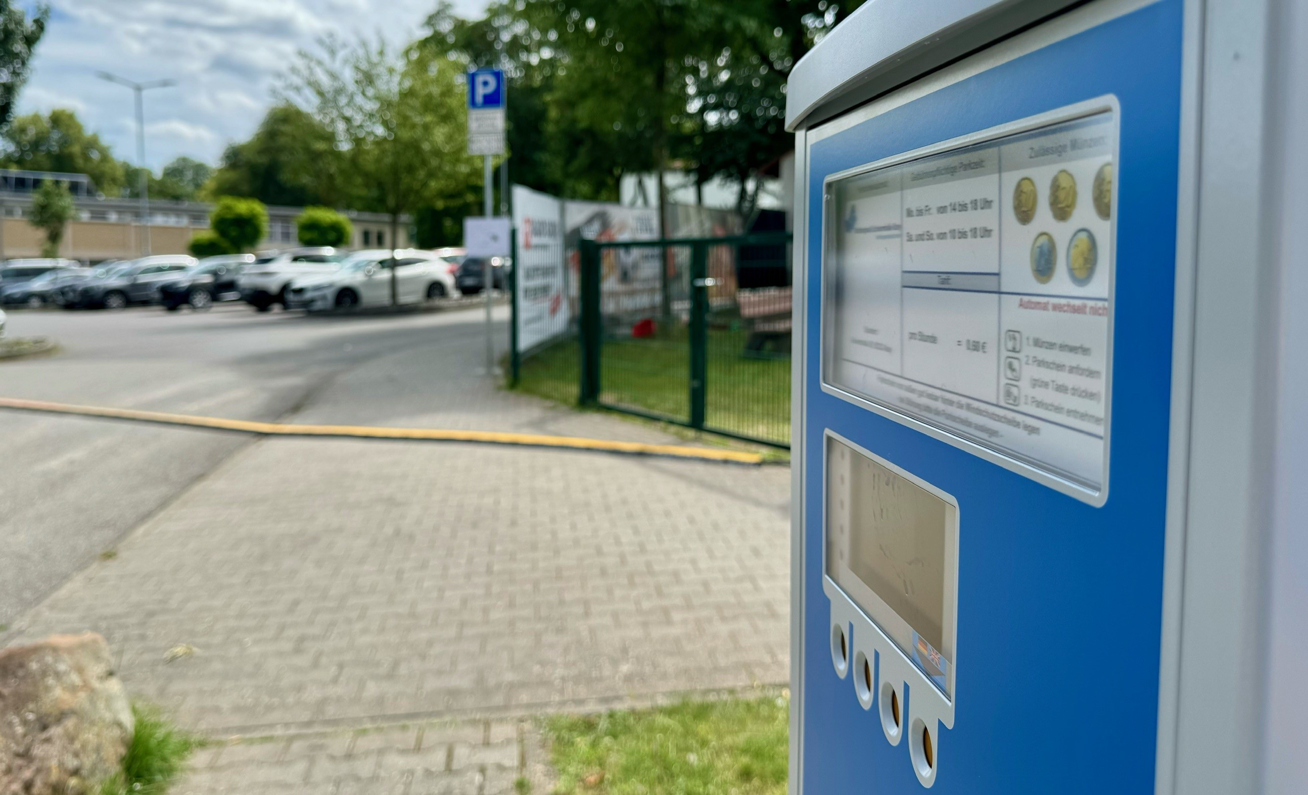 Ein Parkscheinautomat. Im Hintergrund stehen Autos vor dem Eingangsbereich des Wartbergbads.