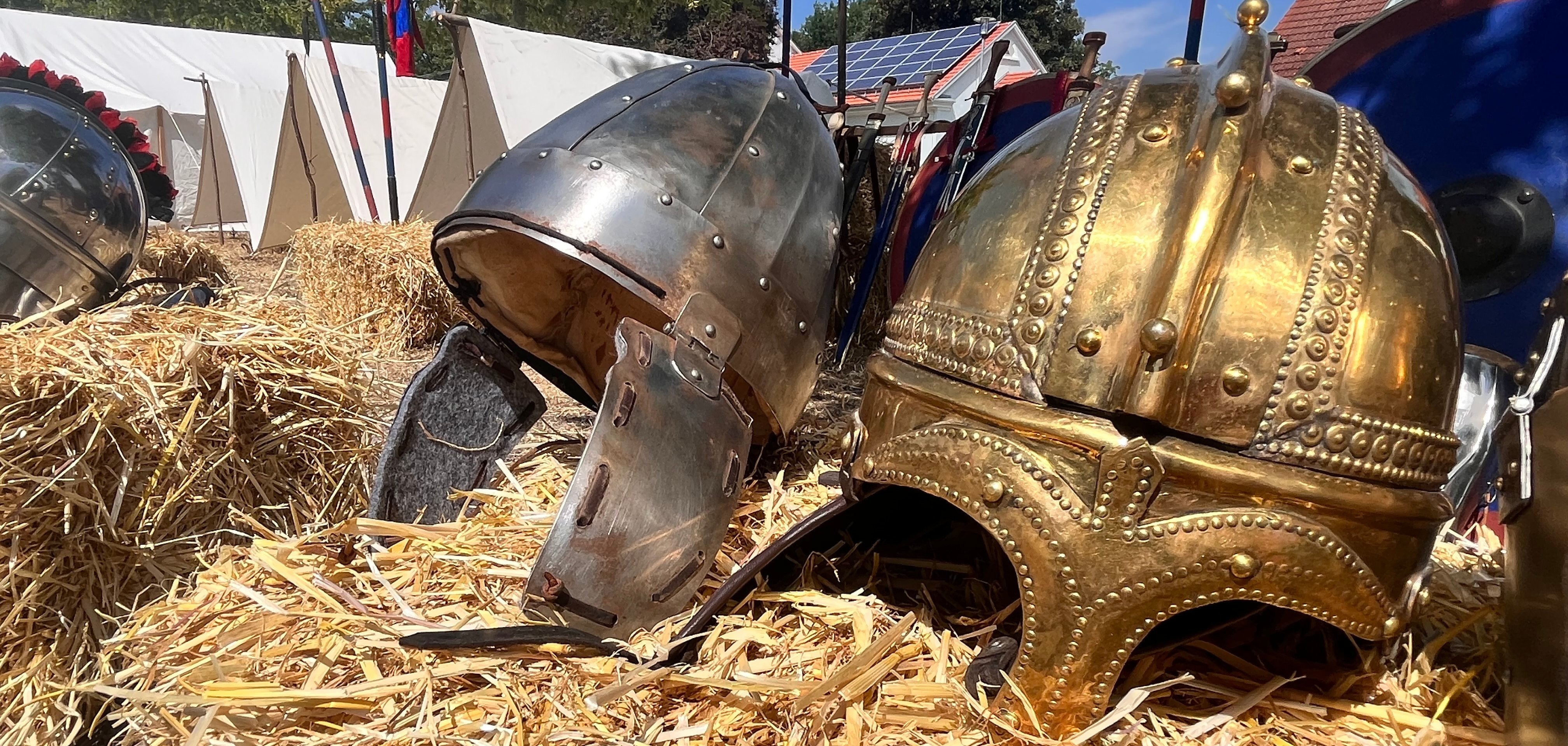 Römische Metallhelme liegen auf einem Strohballen.