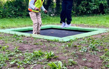 Zwei Kinder hüpfen auf einem im Gras eingelassenen Bodentrampolin.