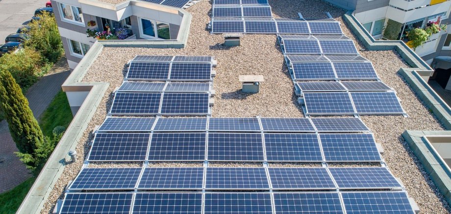 Ein Dach eines Mehrfamilienhauses mit zahlreichen Solarplatten aus der Luft fotografiert.