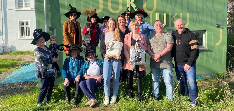 Frauen mit Hexenhüten und das JUKU-Team vor der grünen Wand des Neubaus des JUKU.