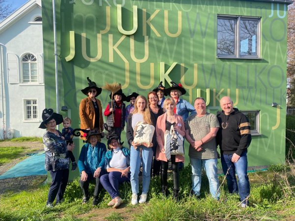 Frauen mit Hexenhüten und das JUKU-Team vor der grünen Wand des Neubaus des JUKU.