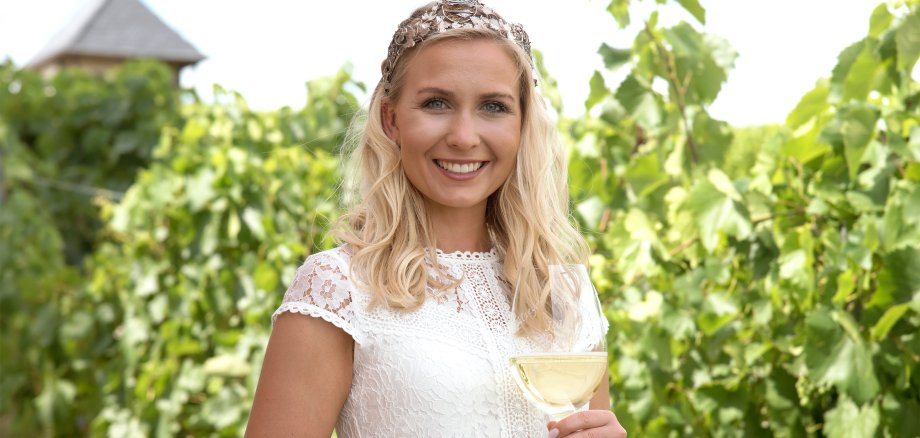 Eine Weinkönigin mit Krone und Weinglas in den sommergrünen Weinbergen.
