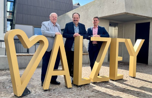 Armin Burkart, Johann Lafer und Bürgermeister Steffen Jung stehen hinter dem Fotopoint auf dem Museumsplatz, der aus goldenen Buchstaben "I love Alzey" formt.