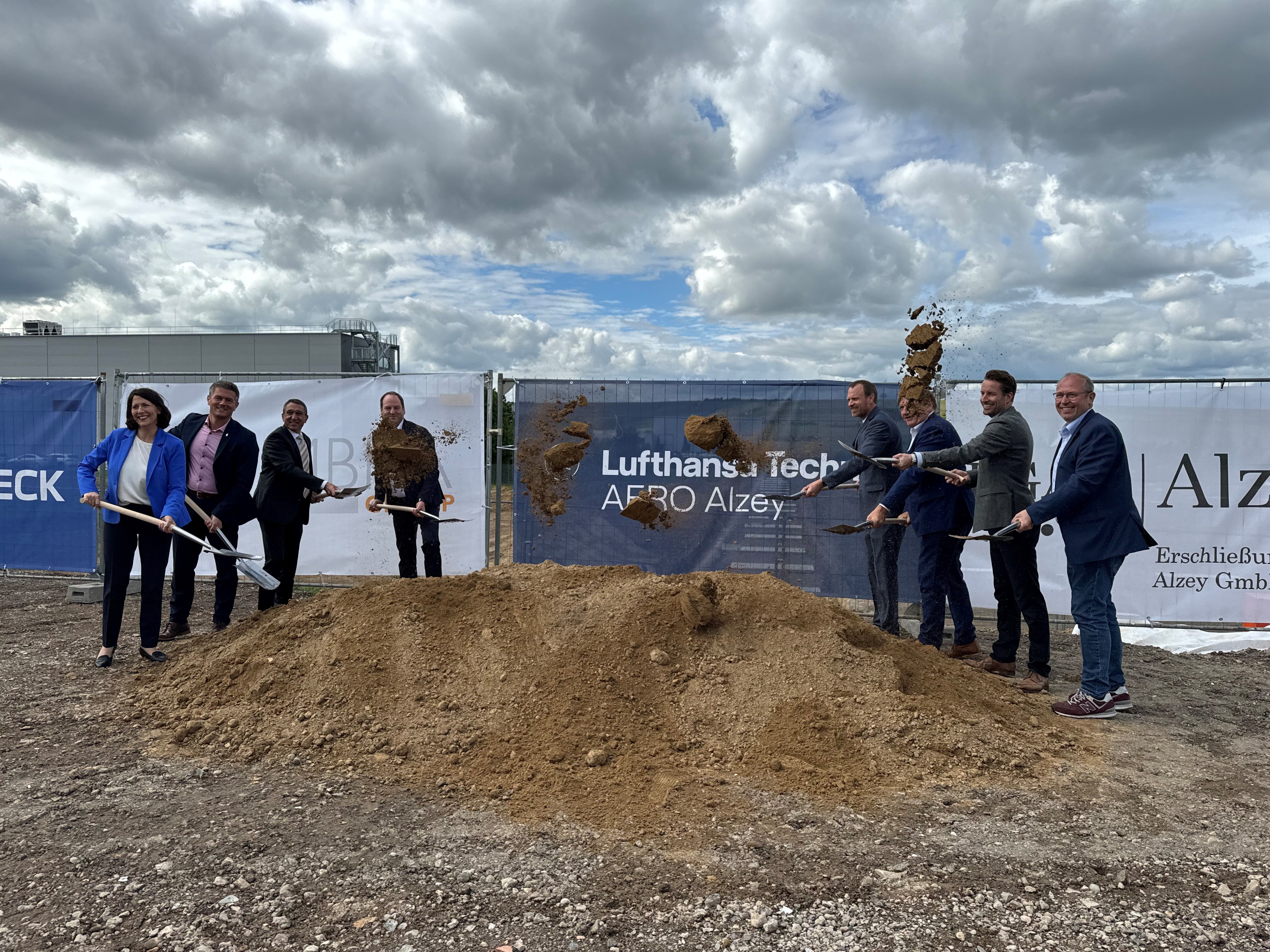 Acht Personen stehen um einen Erdhaufen und werfen mit Spaten Erde in die Luft.