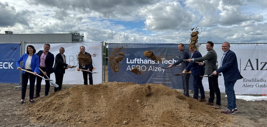 Acht Personen stehen um einen Erdhaufen und werfen mit Spaten Erde in die Luft.