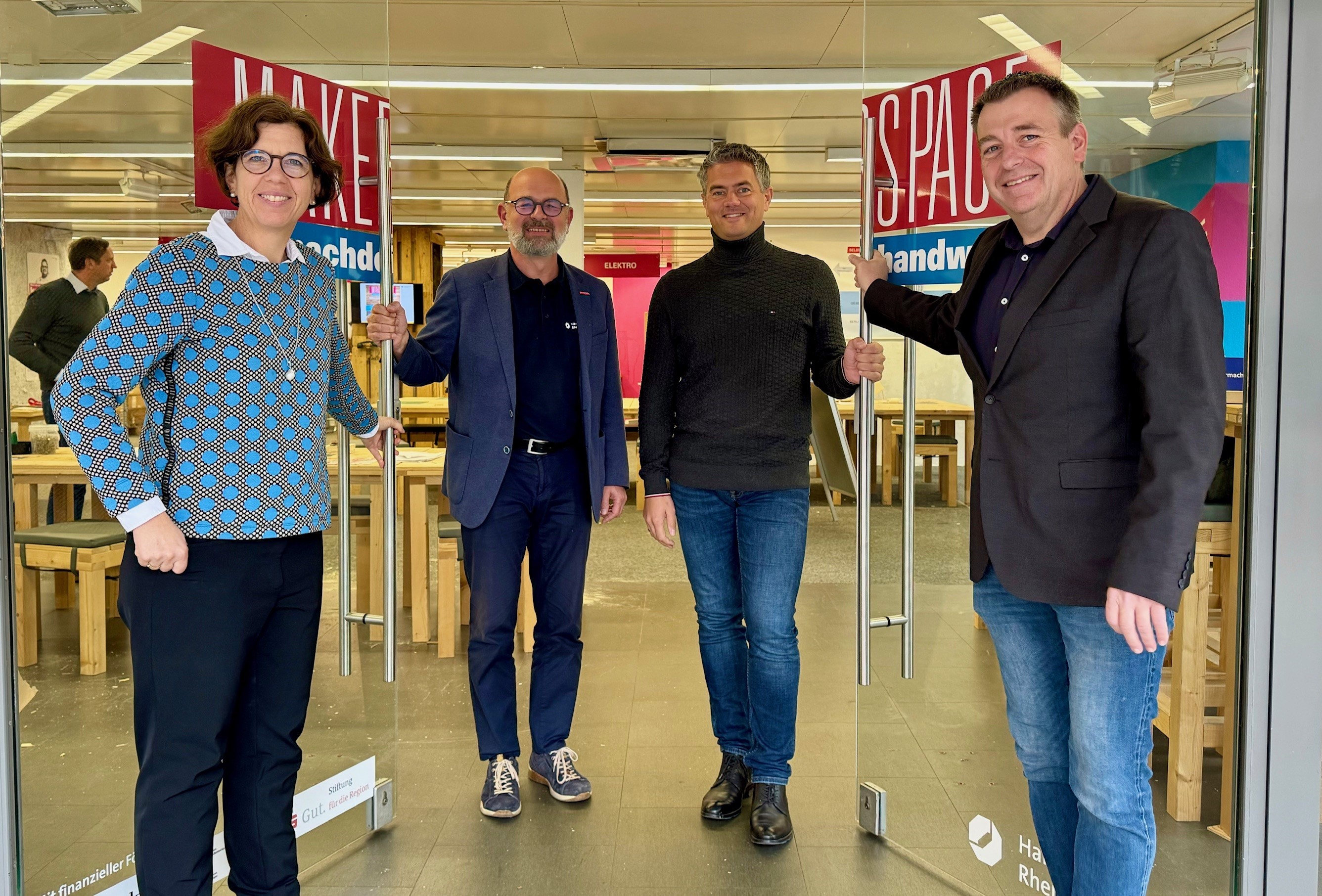 Vier Personen stehen vor einer offenen Glastür zu einem Raum mit zahlreichen Holzmöbeln.