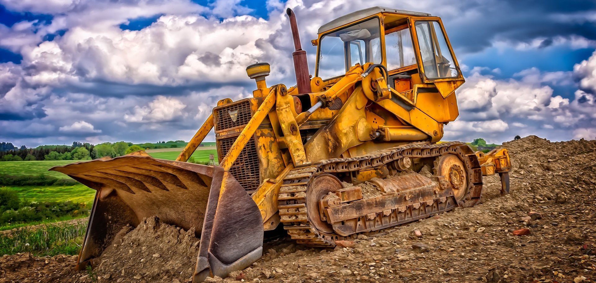 Ein großes gelbes Baugerät mit Schaufel arbeitet sich durch die Baustelle.