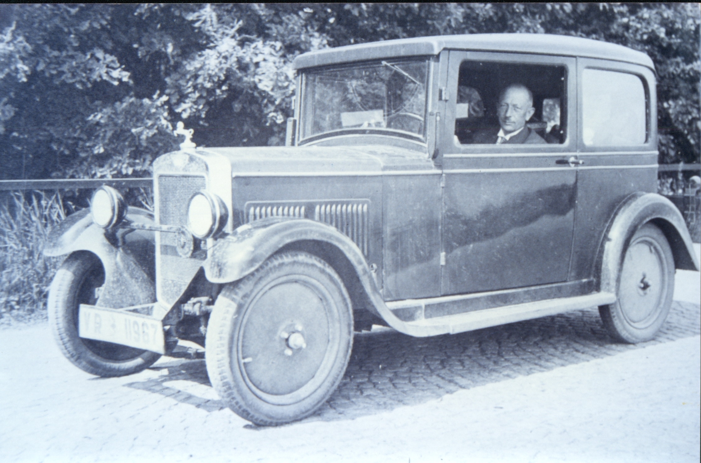 Eine Schwarz-Weiß-Aufnahme eines Mannes in einem sehr alten Auto.