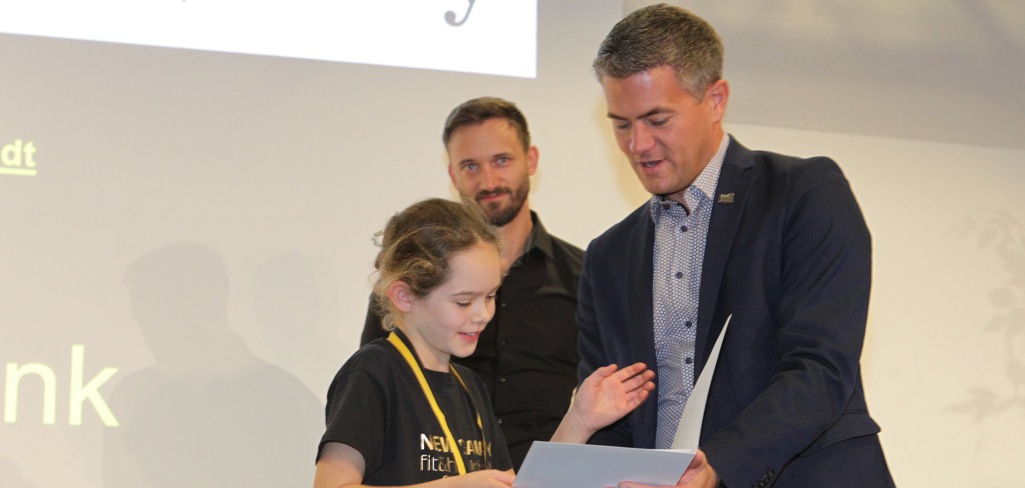 Ein Mann überreicht einem jungen Mädchen eine Urkunde.