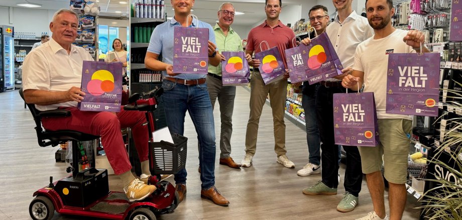 Mehrere Personen halten in einem Supermarkt bunte Papiertüten mit dem Wort Vielfalt hoch