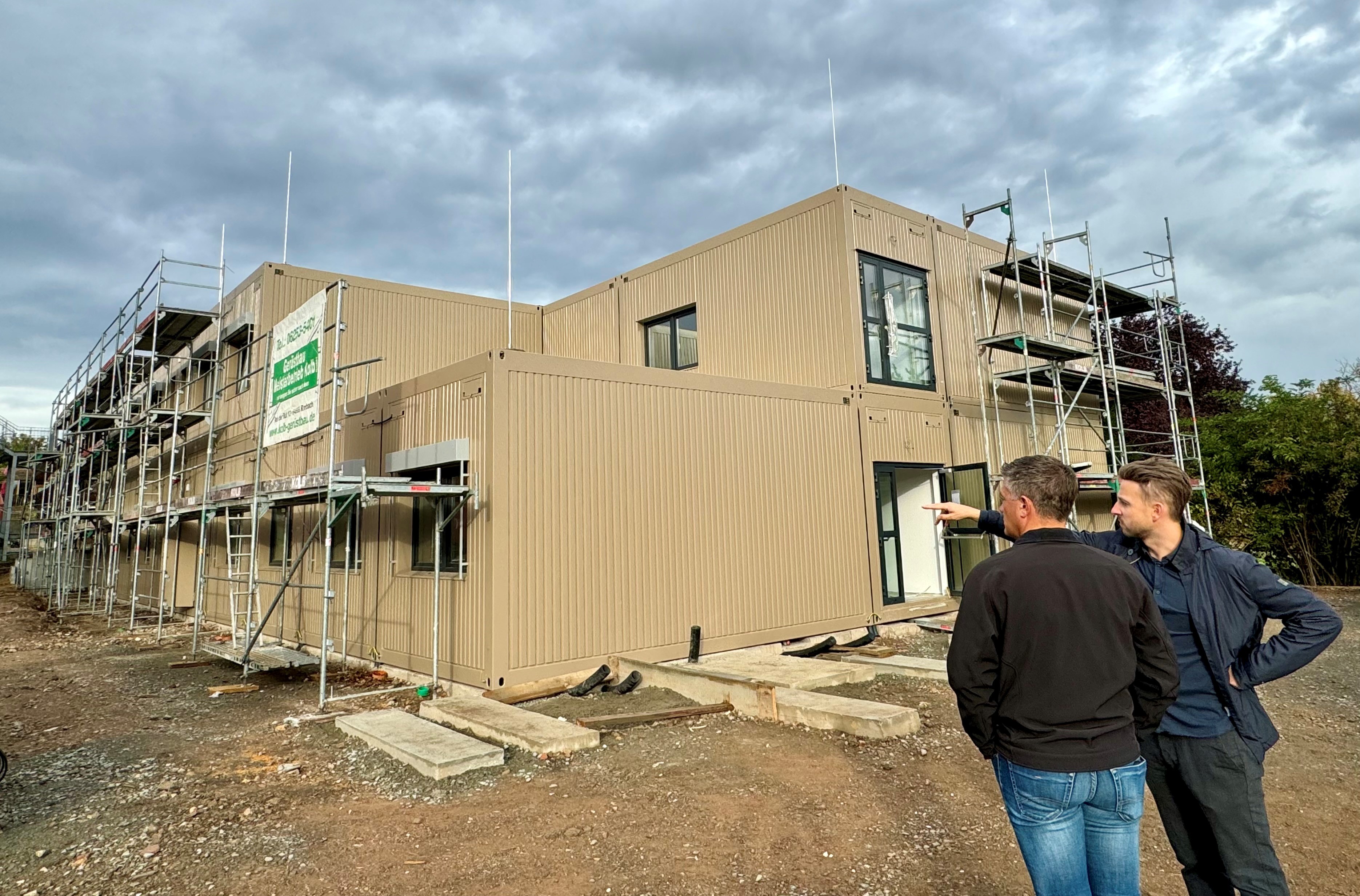 Zwei Personen stehen vor den beigen Schulcontainern, in denen nach den Ferien der Unterricht an der ASS stattfinden soill.