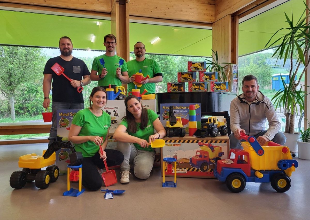4 Personen im grünen Tshirt und 2 Männer mit vielen Spielsachen um sie herum