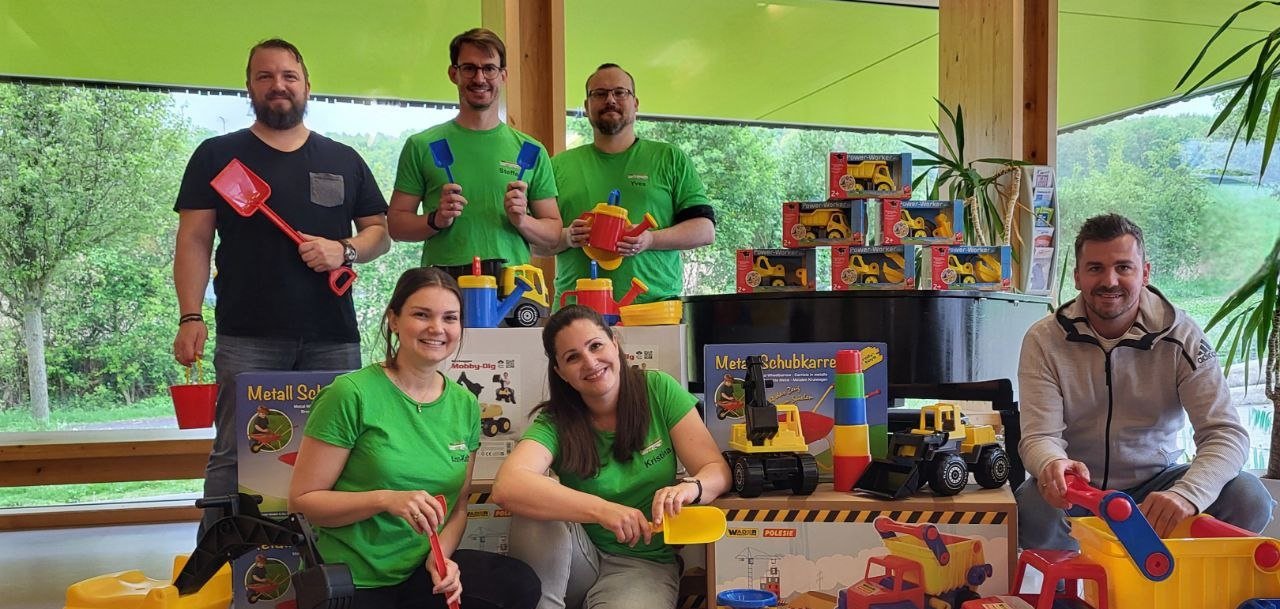 4 Personen im grünen Tshirt und 2 Männer mit vielen Spielsachen um sie herum