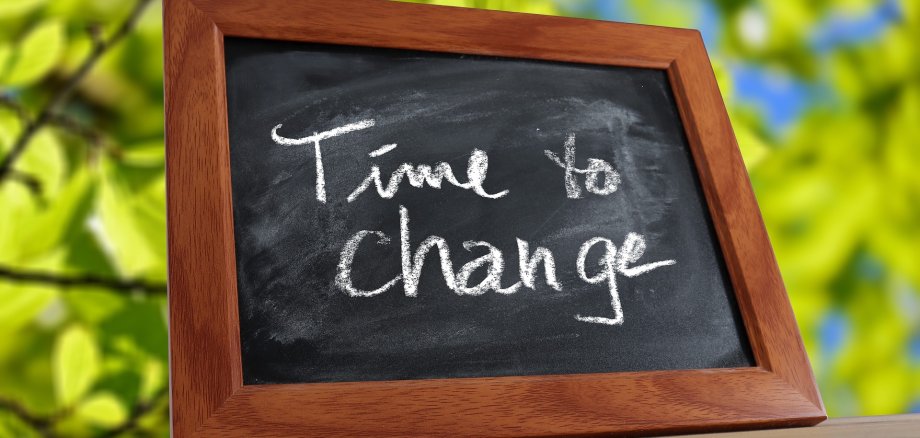 "Time to Change" Tischtafel (Schild) auf einem Holztisch im Freien. (Blätter der Baume sind im Hintergrund zu sehen)