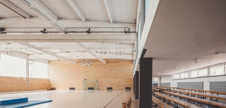 Eine leere Turn/Sporthalle, es ist ein Tor zusehen und einige Bänke.