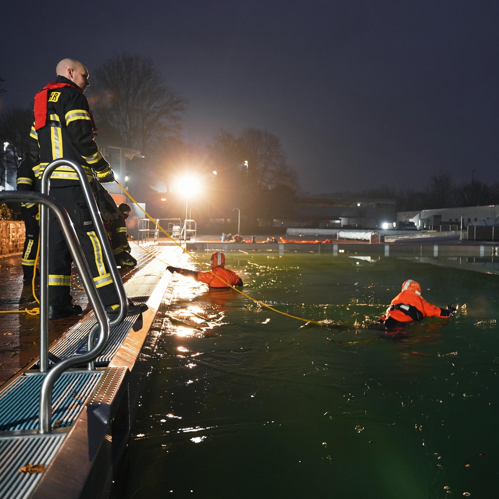 Feuerwehrleute halten orange angezogene Menschen die im grünen Wasser schwimmen