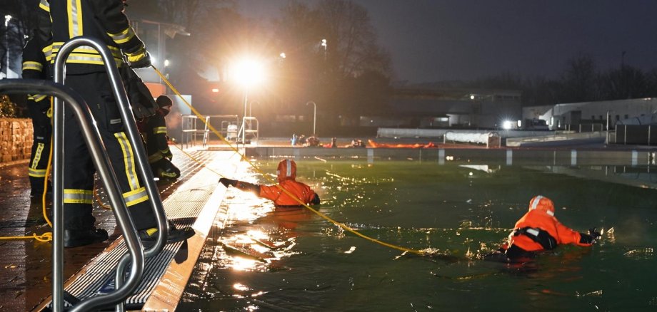 Feuerwehrleute halten orange angezogene Menschen die im grünen Wasser schwimmen
