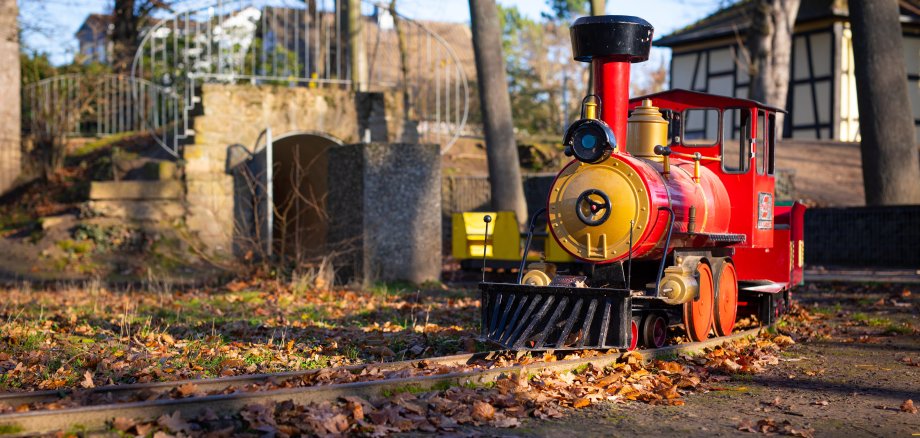 eine rote Lokomotive für Kinder auf dem Spielplatz bei herbstlichem Wetter voller brauner Blätter