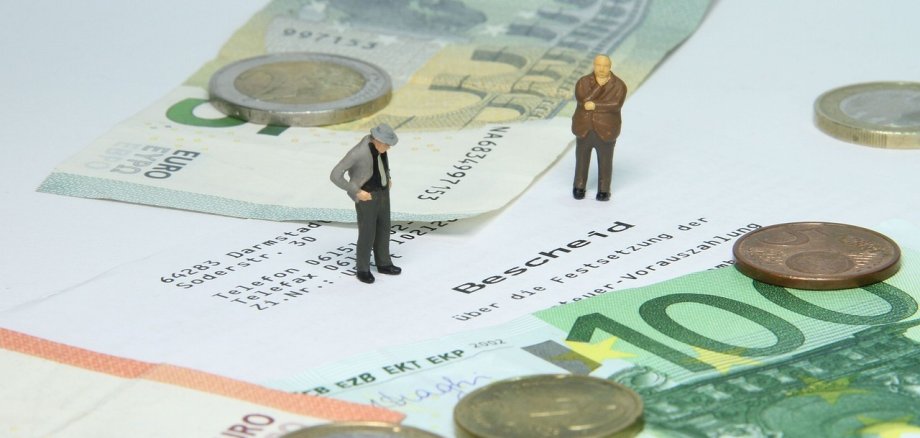 2 Menschliche mini Figuren stehen auf einem Bescheid und außen liegt Geld
