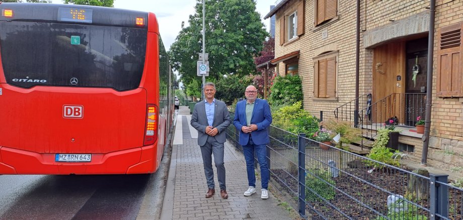 2 Männer stehen vor einer Bushaltestelle neben einem Bu