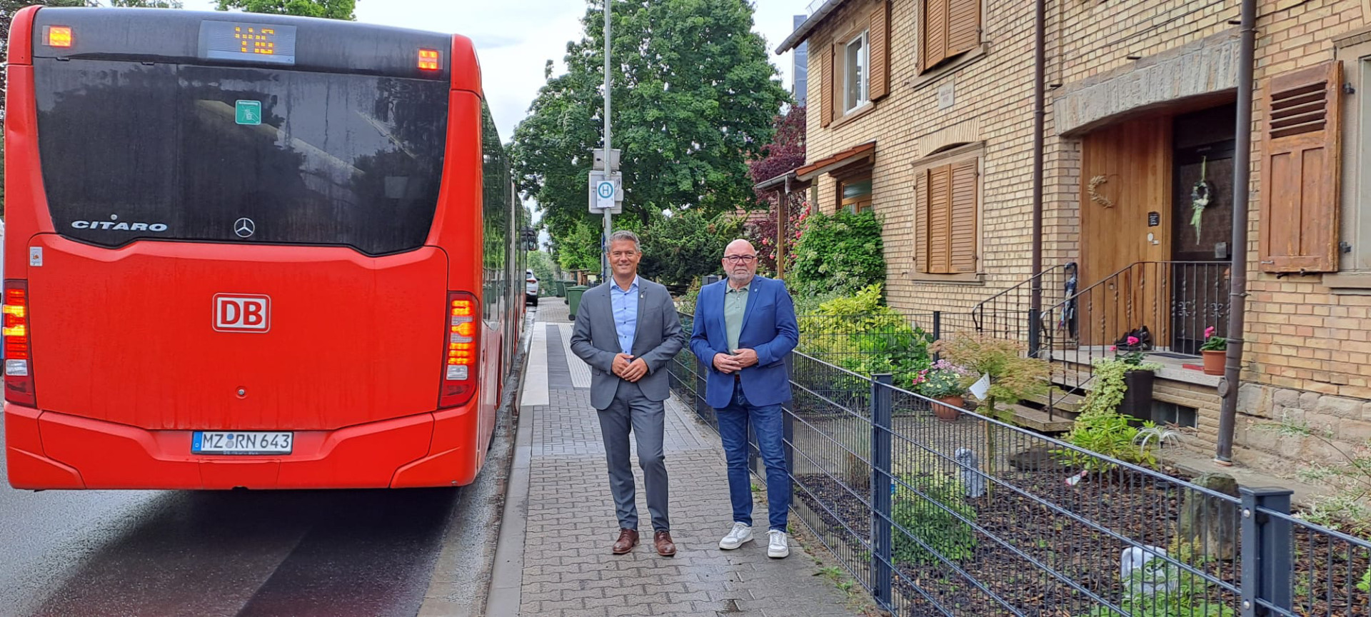 2 Männer stehen vor einer Bushaltestelle neben einem Bu