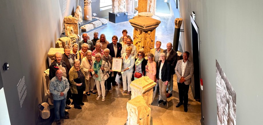 viele Menschen in der Steinhalle des Museums und einer mit einer Urkunde eingerahmt