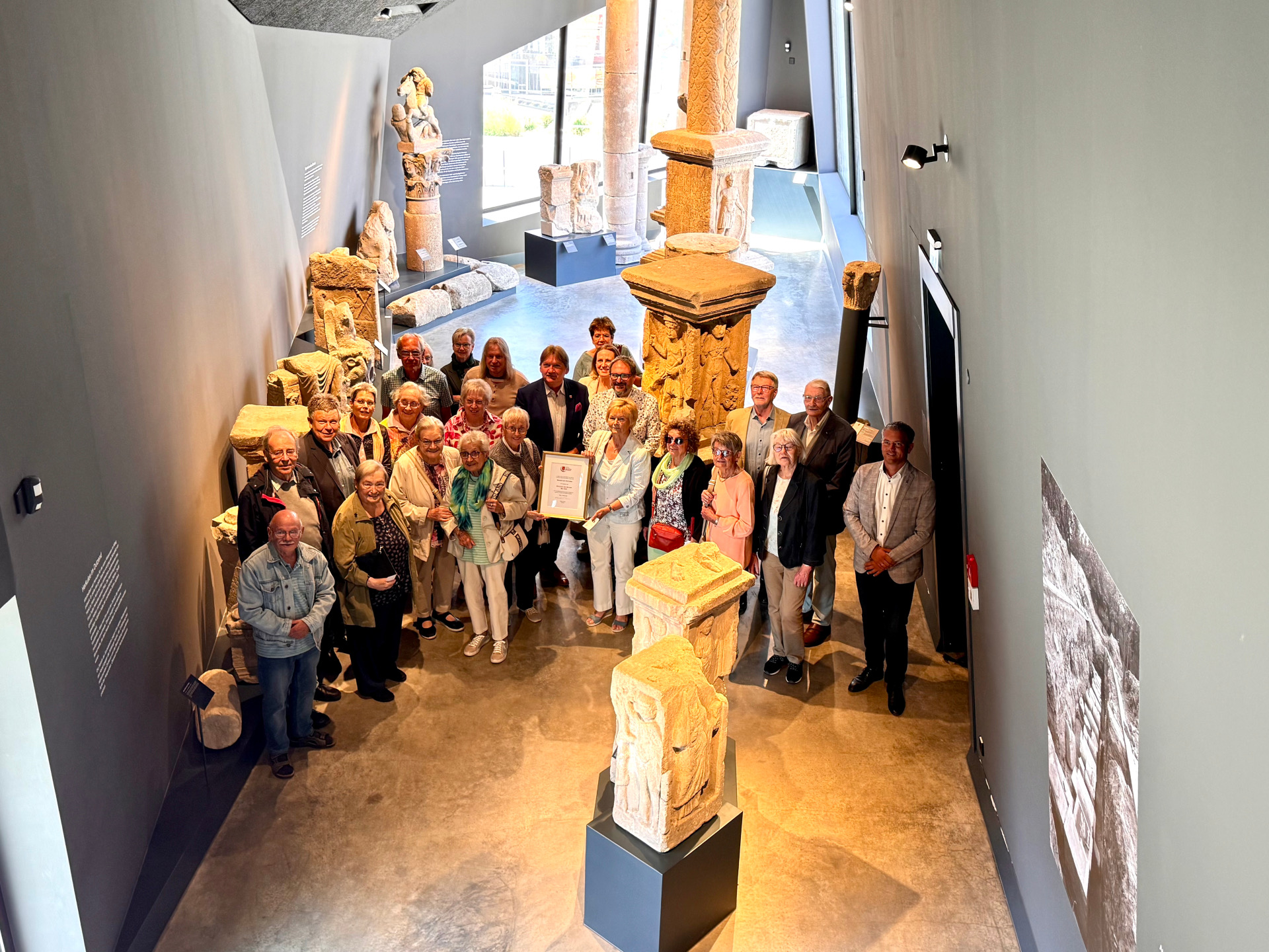 viele Menschen in der Steinhalle des Museums und einer mit einer Urkunde eingerahmt