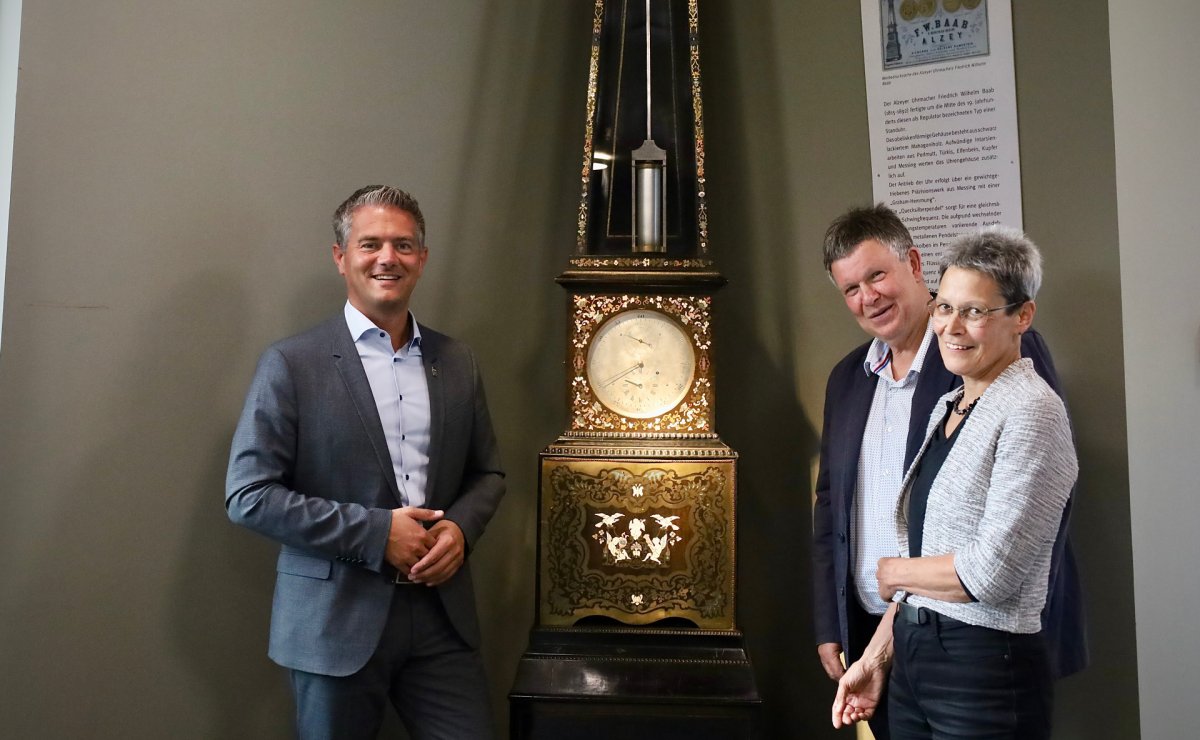 3 Personen stehen vor einer alten Uhr