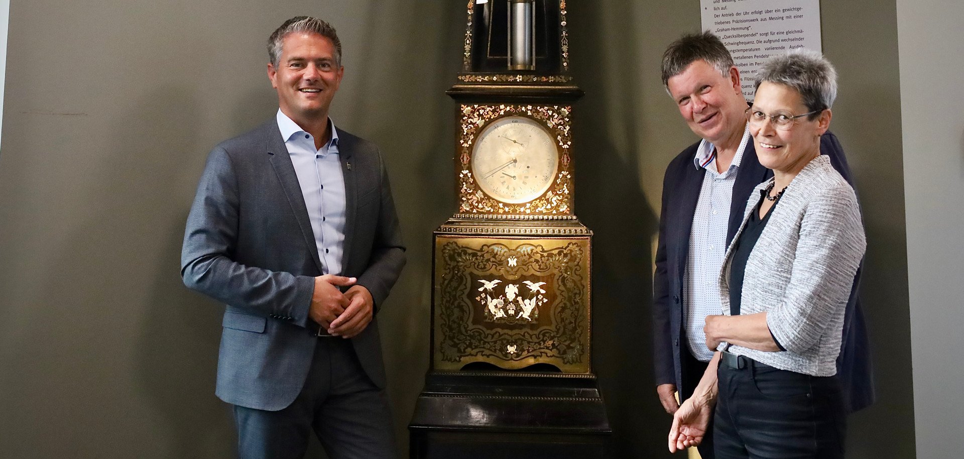 3 Personen stehen vor einer alten Uhr