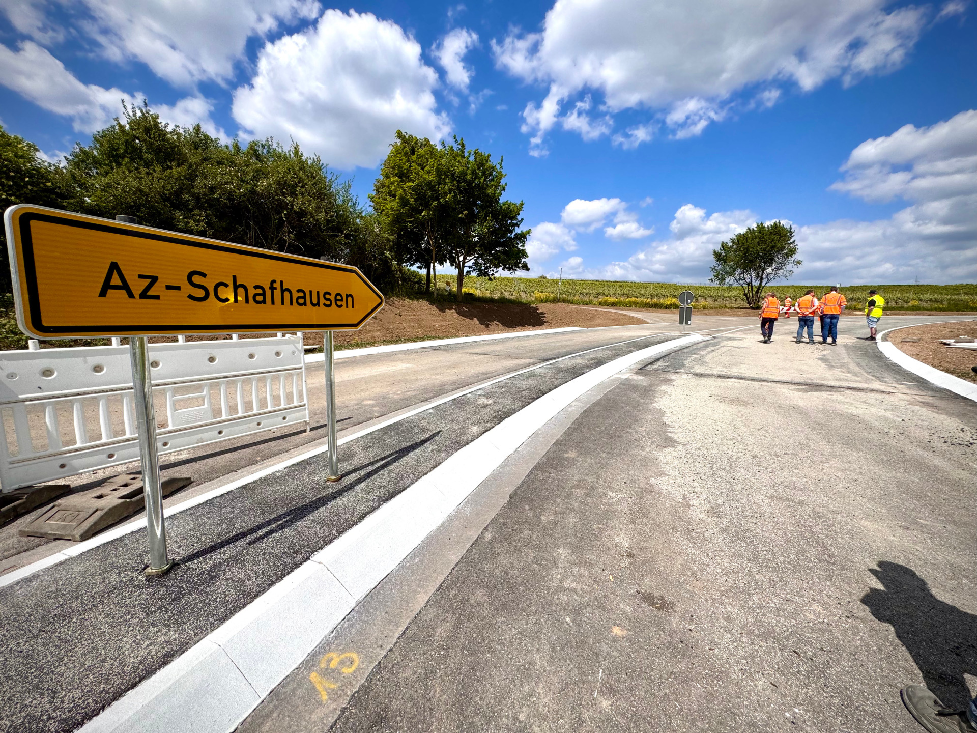 eine neu gebaute Straße mit Arbeitern und einem Schild Richtung Alzey-Schafhausen