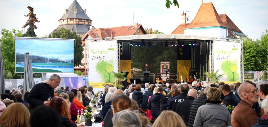 viele Menschen sitzen und auf der Bühne steht der Bürgermeister