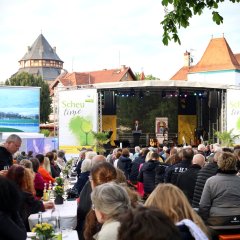 viele Menschen sitzen und auf der Bühne steht der Bürgermeister