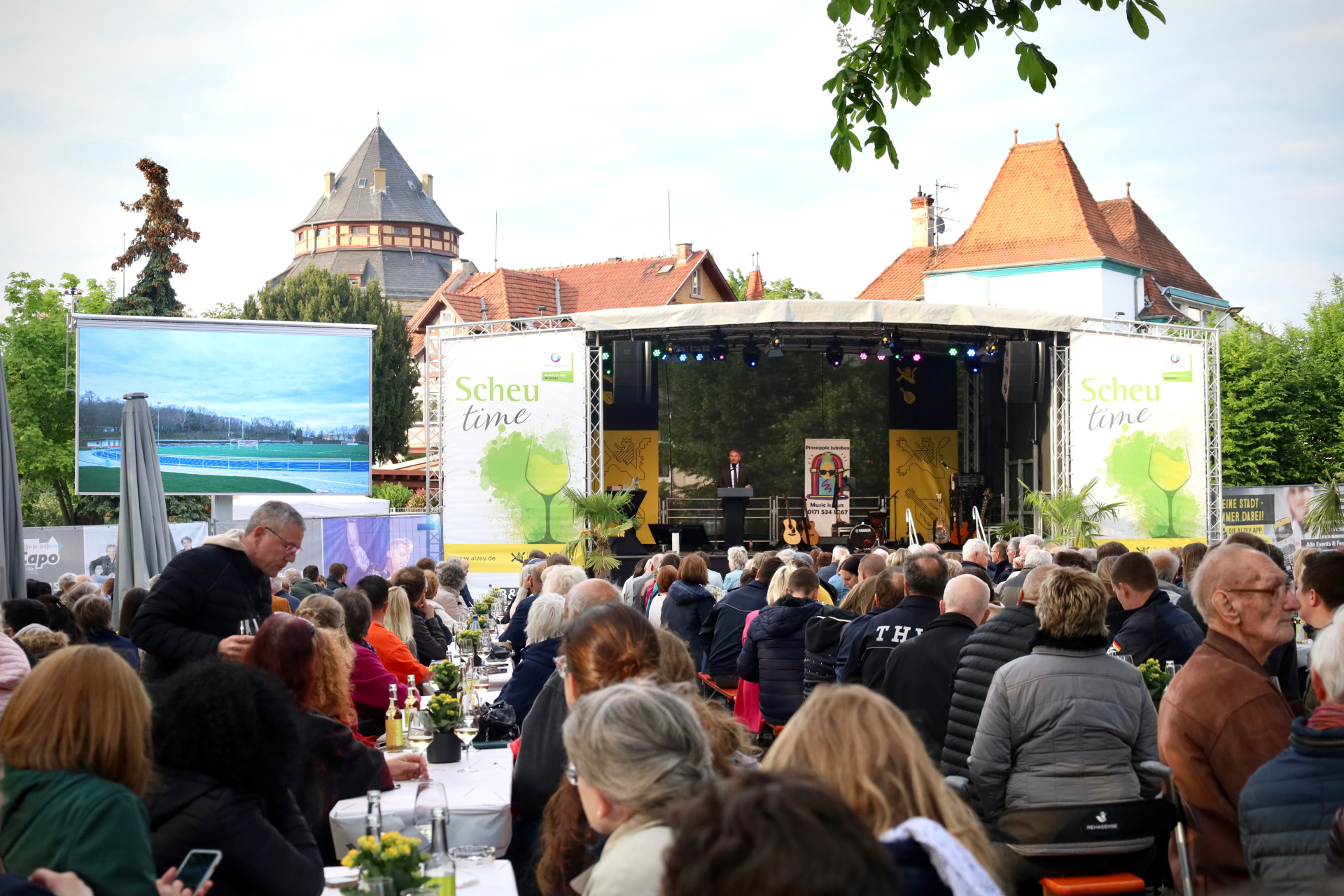viele Menschen sitzen und auf der Bühne steht der Bürgermeister