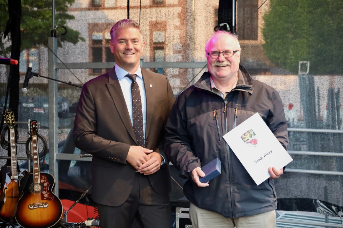 2 Männer stehen und einer hält ein Schmuckkästchen und ein weißes Blatt von der Stadt Alzey
