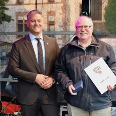 2 Männer stehen und einer hält ein Schmuckkästchen und ein weißes Blatt von der Stadt Alzey