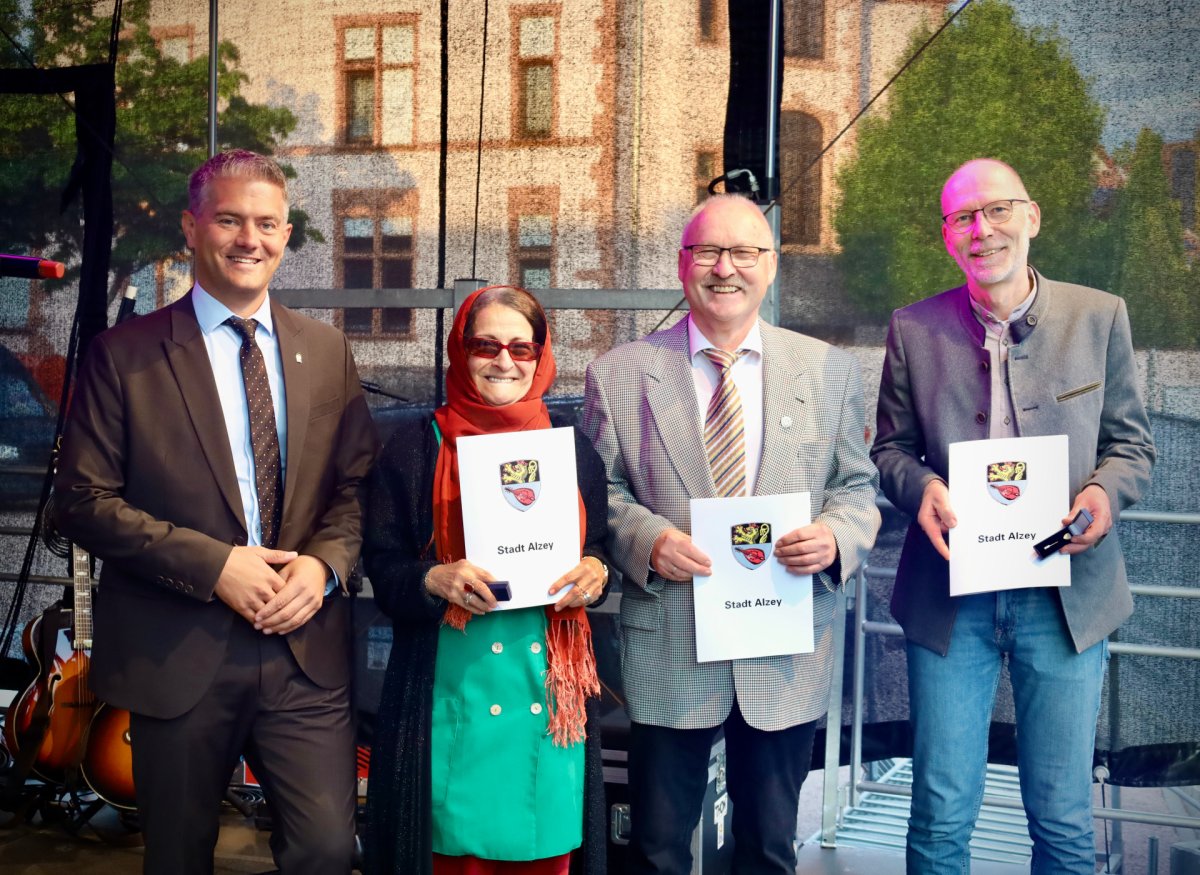 4 Personen stehen und 3 davon halten ein weißes Blatt von der Stadt Alzey