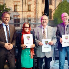 4 Personen stehen und 3 davon halten ein weißes Blatt von der Stadt Alzey