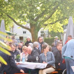 viele Personen sitzen an Holztischen und auf Sitzbänken und einige stehen/laufen