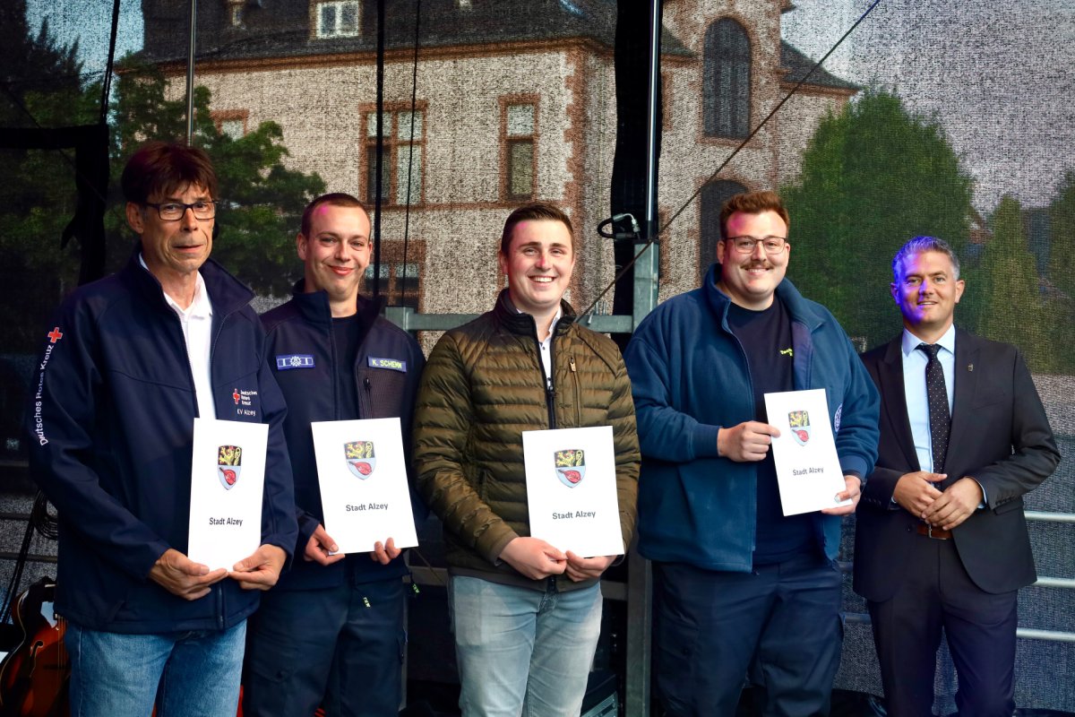 5 Männer stehen und 4 von denen halten ein weißes Papier von der Stadt Alzey