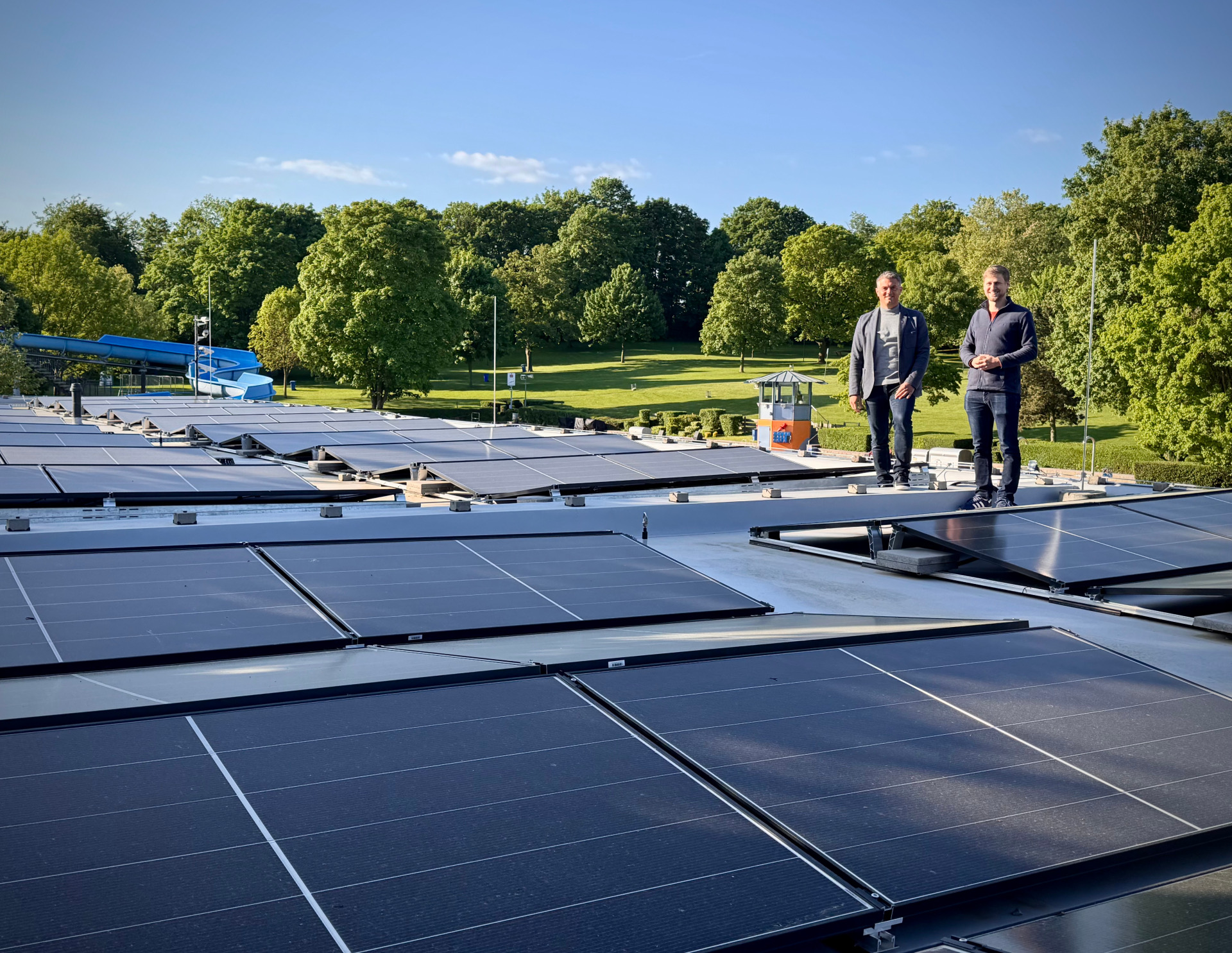3 Männer stehen bei Solarplatten im Hintergrund ist die Schwimmbadrutsche