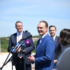 ein Mann redet in 4 Mikrofone rein und außenrum weitere Personen am zugucken