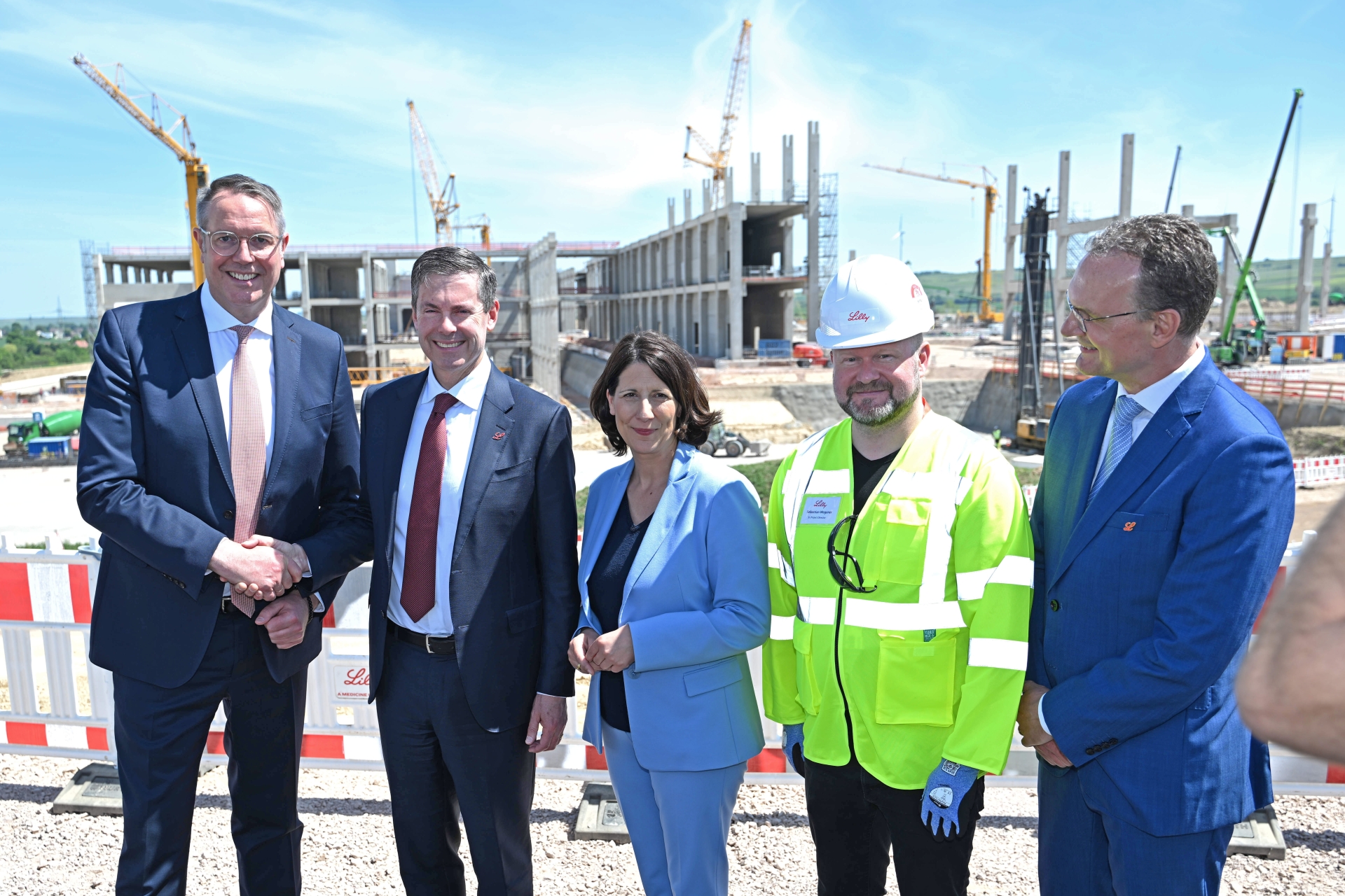 4 Männer und eine Frau im Anzug und einer in Baustellenkleidung, 2 davon schütteln sich die Hände