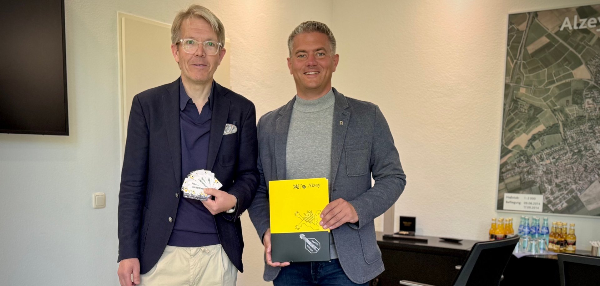 2 Männer präsentieren Neubürgermappen in der Farbe geld/schwarz