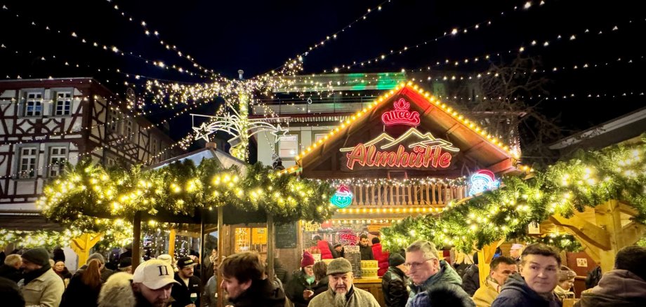 Besucher des Alzeyer Weihnachtsmarkt vor der hell leuchtenden Hütte.