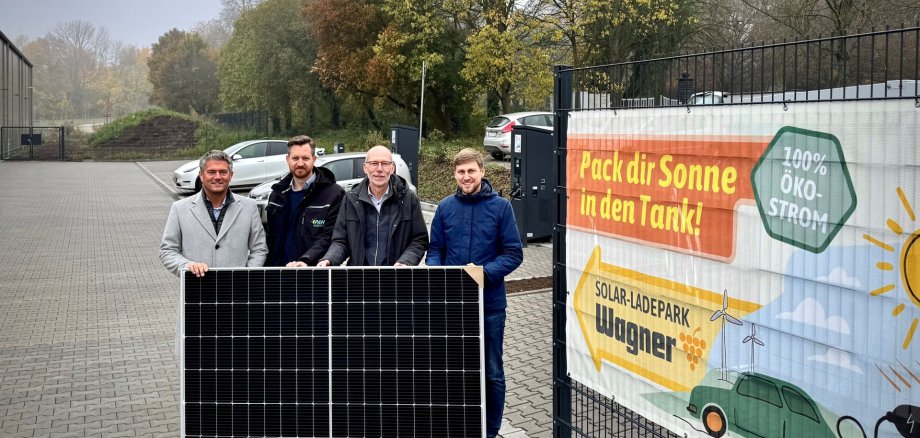 vier Personen halten zusammen ein Photovoltaik Paneel fest.